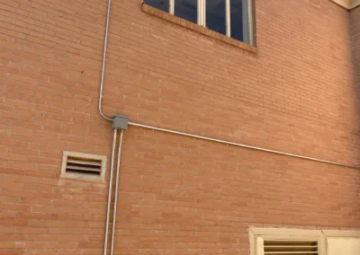 A brick building wall with electrical conduits and a window.
